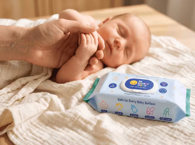 Parent holding a sleeping newborn's hand next to a Kinder Clean wipes pack