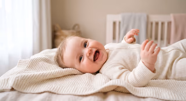 Happy baby laughing on a soft blanket in the nursery