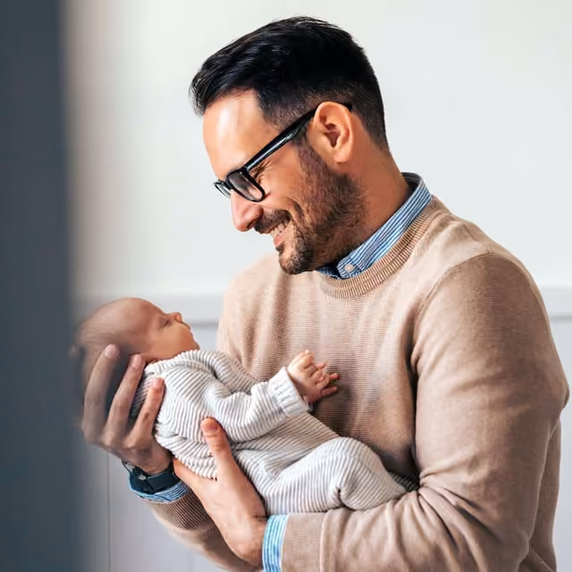 Parent lifting a baby into the air in a green open field